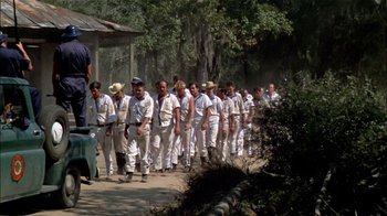 Movie still from “The Longest Yard” (1974), directed by Robert Aldrich – A large group of men in white suits are walking down the street; Wide shot, Low angle