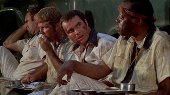 Movie still from “The Longest Yard” (1974), directed by Robert Aldrich – A group of men sitting next to each other on a table; Medium shot, Low angle