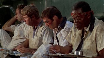 Movie still from “The Longest Yard” (1974), directed by Robert Aldrich – A group of men sitting next to each other on a table; Medium shot, Low angle