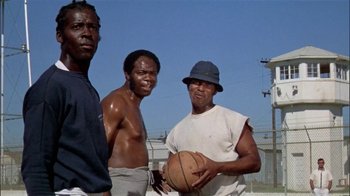 Movie still from “The Longest Yard” (1974), directed by Robert Aldrich – A group of men standing next to each other holding a basketball; Medium shot, Low angle