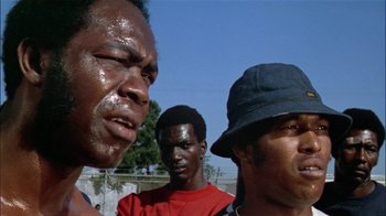 Movie still from “The Longest Yard” (1974), directed by Robert Aldrich – A group of men standing next to each other in front of a chain link fence; Close Up shot, Low angle