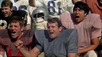 Movie still from “The Longest Yard” (1974), directed by Robert Aldrich – A group of football players in the stands yelling; Medium shot, Low angle