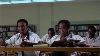 Movie still from “The Longest Yard” (1974), directed by Robert Aldrich – A group of men sitting at a table in a library; Medium shot, Low angle