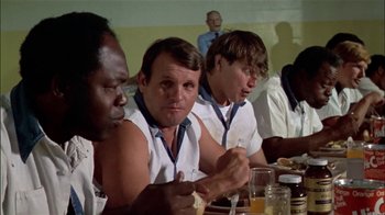 Movie still from “The Longest Yard” (1974), directed by Robert Aldrich – A group of people sitting at a table eating; Medium shot, Low angle