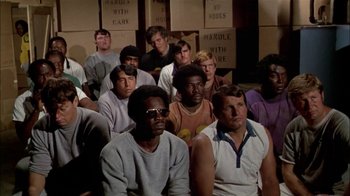 Movie still from “The Longest Yard” (1974), directed by Robert Aldrich – A group of men sitting in front of each other in a room; Medium shot, High angle