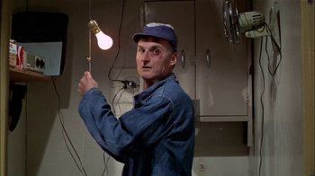 Movie still from “The Longest Yard” (1974), directed by Robert Aldrich – A man in a blue work shirt holding a light; Medium shot, Low angle