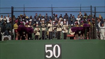 Movie still from “The Longest Yard” (1974), directed by Robert Aldrich – A group of people standing on top of a green field; Extreme Wide shot, High angle