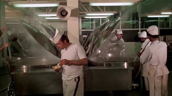 Movie still from “The Longest Yard” (1974), directed by Robert Aldrich – A man in white shirt standing in a kitchen next to a pan; Wide shot, Low angle