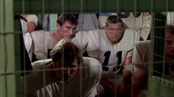Movie still from “The Longest Yard” (1974), directed by Robert Aldrich – A group of football players sitting next to each other; Medium shot, Low angle