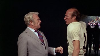 Movie still from “The Longest Yard” (1974), directed by Robert Aldrich – Two older men shaking hands in front of a black background; Medium shot, Over the shoulder angle