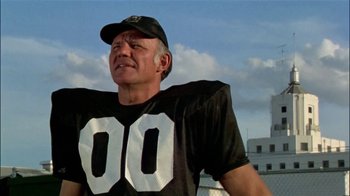 Movie still from “The Longest Yard” (1974), directed by Robert Aldrich – An older man in a football jersey and hat; Close Up shot, Low angle