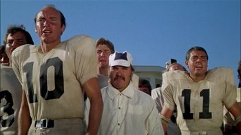 Movie still from “The Longest Yard” (1974), directed by Robert Aldrich – A group of men standing next to each other on a football field; Medium shot, Low angle
