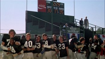 Movie still from “The Longest Yard” (1974), directed by Robert Aldrich – A group of men standing on top of a field; Wide shot, Low angle