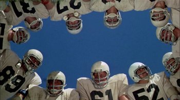 Movie still from “The Longest Yard” (1974), directed by Robert Aldrich – A group of football players are lined up in formation; Wide shot, Overhead angle