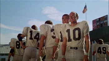 Movie still from “The Longest Yard” (1974), directed by Robert Aldrich – A group of men standing next to each other on top of a football field; Medium shot, Low angle