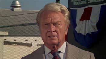 Movie still from “The Longest Yard” (1974), directed by Robert Aldrich – An older man in a gray suit and red neck tie; Close Up shot, Low angle