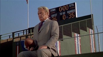 Movie still from “The Longest Yard” (1974), directed by Robert Aldrich – An older man in a suit holding a football; Medium shot, Low angle