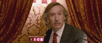 Movie still from “The Look of Love” (2013), directed by Michael Winterbottom – A person wearing a suit and tie; Close Up shot, Over the shoulder angle