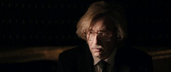 Movie still from “The Look of Love” (2013), directed by Michael Winterbottom – A man in a suit and tie wearing glasses; Close Up shot, Over the shoulder angle