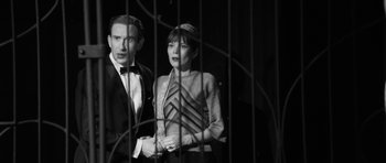 Movie still from “The Look of Love” (2013), directed by Michael Winterbottom – A man and a woman standing next to each other in front of a cage; Medium shot, Over the shoulder angle