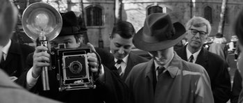 Movie still from “The Look of Love” (2013), directed by Michael Winterbottom – A group of men standing next to each other holding a camera; Medium shot, High angle