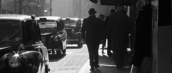 Movie still from “The Look of Love” (2013), directed by Michael Winterbottom – Black and white photograph of a man walking down the street; Wide shot, Low angle