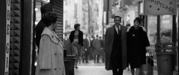 Movie still from “The Look of Love” (2013), directed by Michael Winterbottom – A black and white photo of people walking down the street; Medium shot, Over the shoulder angle