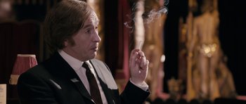 Movie still from “The Look of Love” (2013), directed by Michael Winterbottom – A man in a suit and tie smoking a cigarette; Medium shot, Over the shoulder angle