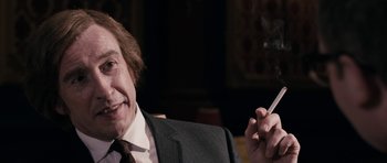 Movie still from “The Look of Love” (2013), directed by Michael Winterbottom – An older man in a suit and tie smoking a cigarette; Close Up shot, Over the shoulder angle