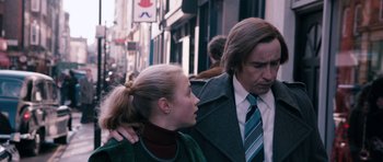 Movie still from “The Look of Love” (2013), directed by Michael Winterbottom – A man and a woman standing next to each other on the street; Medium shot, Over the shoulder angle