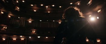 Movie still from “The Look of Love” (2013), directed by Michael Winterbottom – A person standing in a theater with lights on; Wide shot, Over the shoulder angle