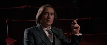 Movie still from “The Look of Love” (2013), directed by Michael Winterbottom – A man in a suit and tie smoking a cigarette in a theater; Medium shot, Low angle