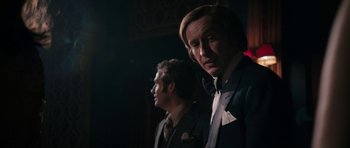Movie still from “The Look of Love” (2013), directed by Michael Winterbottom – A man in a suit standing next to another man in a suit; Medium shot, Over the shoulder angle