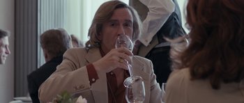 Movie still from “The Look of Love” (2013), directed by Michael Winterbottom – A man drinking a glass of wine at a table; Close Up shot, Over the shoulder angle