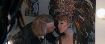 Movie still from “The Look of Love” (2013), directed by Michael Winterbottom – A man kissing a woman's forehead in front of an elaborate headdress; Close Up shot, Over the shoulder angle