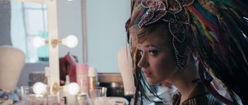 Movie still from “The Look of Love” (2013), directed by Michael Winterbottom – A woman in a colorful headdress looking into a mirror; Close Up shot, Over the shoulder angle