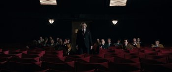 Movie still from “The Look of Love” (2013), directed by Michael Winterbottom – A man in a suit standing in front of a group of people; Wide shot, Low angle