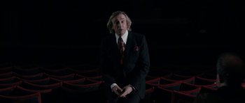 Movie still from “The Look of Love” (2013), directed by Michael Winterbottom – A man wearing a suit and tie in a theater; Medium shot, Low angle