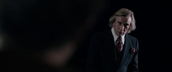 Movie still from “The Look of Love” (2013), directed by Michael Winterbottom – A man in a black suit and a red tie; Close Up shot, Over the shoulder angle