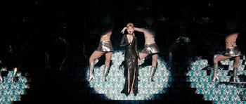 Movie still from “The Look of Love” (2013), directed by Michael Winterbottom – A woman standing in front of a wall with two women standing on either side of her; Wide shot, High angle