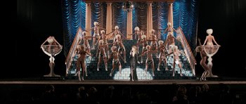 Movie still from “The Look of Love” (2013), directed by Michael Winterbottom – A group of dancers performing on a stage with a woman in a black dress; Extreme Wide shot, High angle