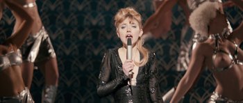 Movie still from “The Look of Love” (2013), directed by Michael Winterbottom – A woman holding a microphone in her hand; Medium shot, Low angle