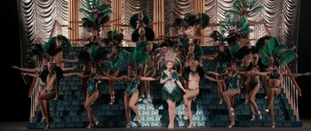 Movie still from “The Look of Love” (2013), directed by Michael Winterbottom – A group of women dressed in costumes and dancing on a stage; Extreme Wide shot, High angle