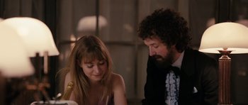 Movie still from “The Look of Love” (2013), directed by Michael Winterbottom – A man and a woman sitting next to each other at a table; Medium shot, Over the shoulder angle