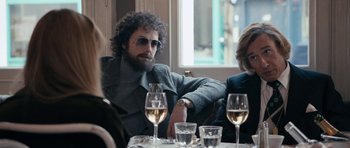 Movie still from “The Look of Love” (2013), directed by Michael Winterbottom – A man sitting at a table with a glass of white wine; Medium shot, Over the shoulder angle