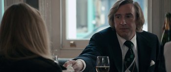 Movie still from “The Look of Love” (2013), directed by Michael Winterbottom – A man sitting at a table with a glass of white wine; Close Up shot, Over the shoulder angle