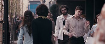Movie still from “The Look of Love” (2013), directed by Michael Winterbottom – A group of people standing on the sidewalk; Medium shot, Over the shoulder angle