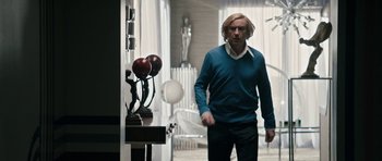 Movie still from “The Look of Love” (2013), directed by Michael Winterbottom – A man in a blue sweater walking in a room; Medium shot, Low angle