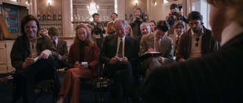 Movie still from “The Look of Love” (2013), directed by Michael Winterbottom – A group of people sitting in a room; Medium shot, Over the shoulder angle
