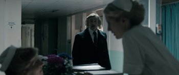 Movie still from “The Look of Love” (2013), directed by Michael Winterbottom – A man standing in front of a mirror in a room; Medium shot, Over the shoulder angle